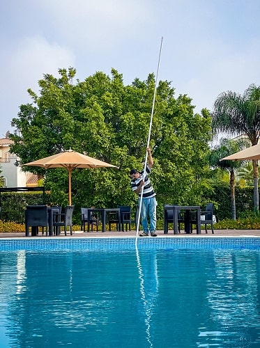 man is cleaning the pool with long stick