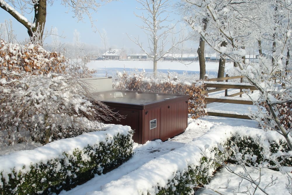 cold snow-covered ground surrounds a closed hot tub